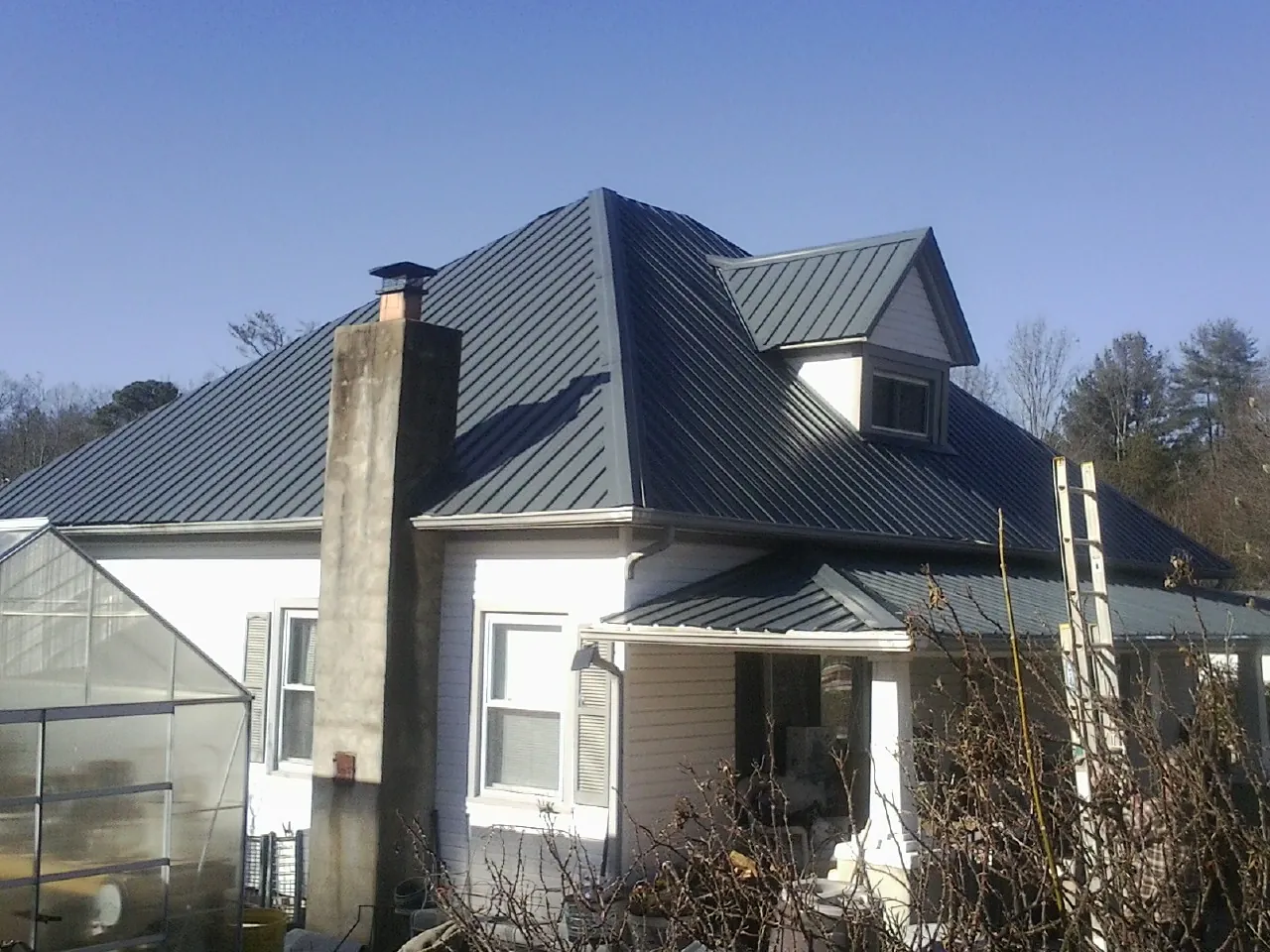 Dark blue standing seam metal roof on a white farmhouse with dormer — Slate & Tile Roof Repair by Roofing Brothers in Alger