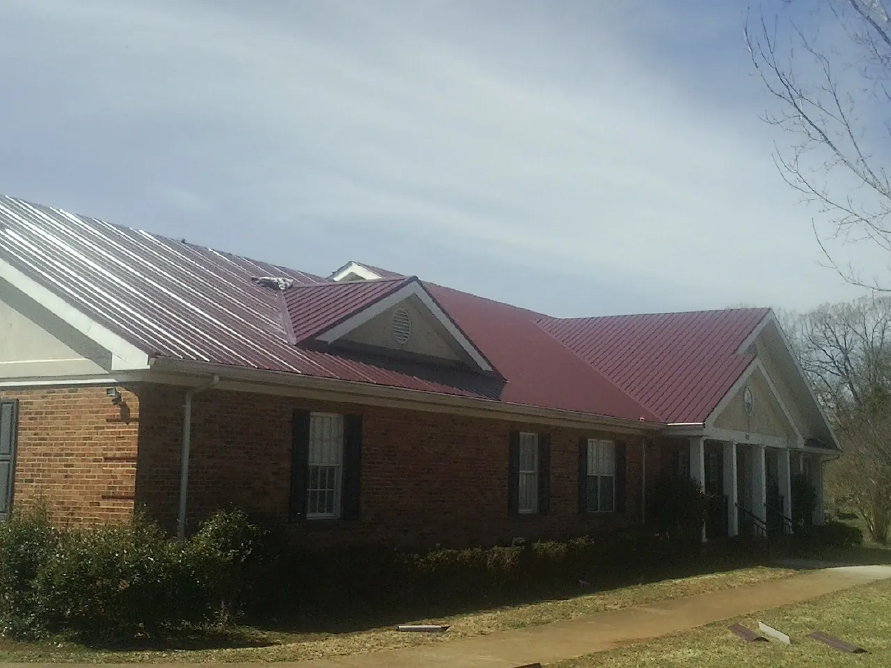 Red metal roof with gabled entries on a long brick building, from a Hail Damage Roof Repair job in Alger