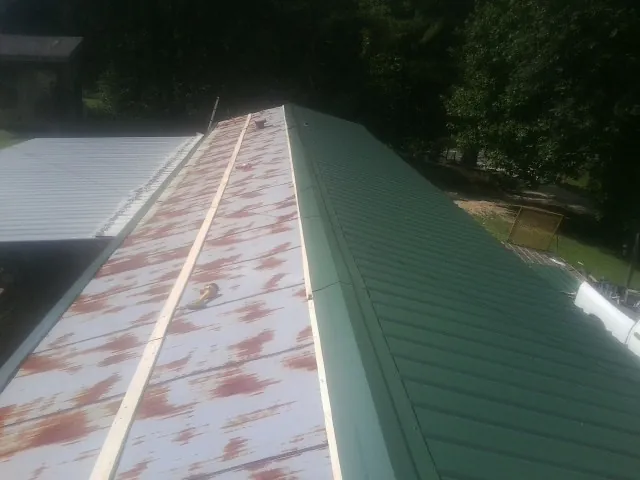 Old rusted panels beside newly installed green metal roofing — Wind Damage Roof Repair by Roofing Brothers in Alger