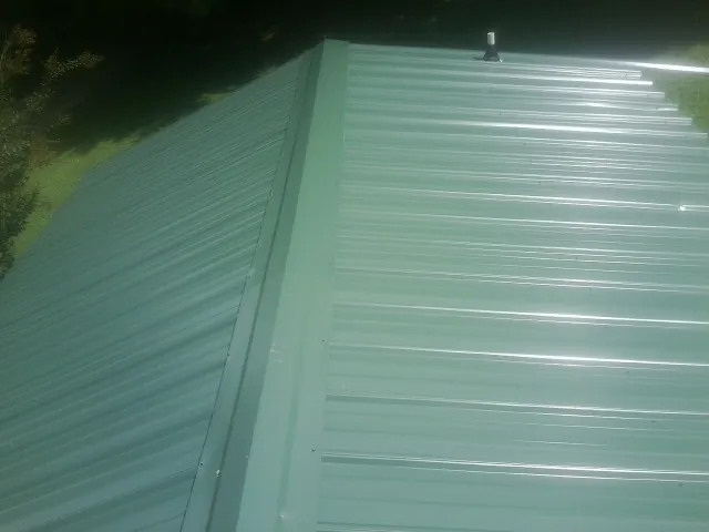 New green metal panels meeting at the ridge of a roof — Flat Roof Repair work by our crew in Alger