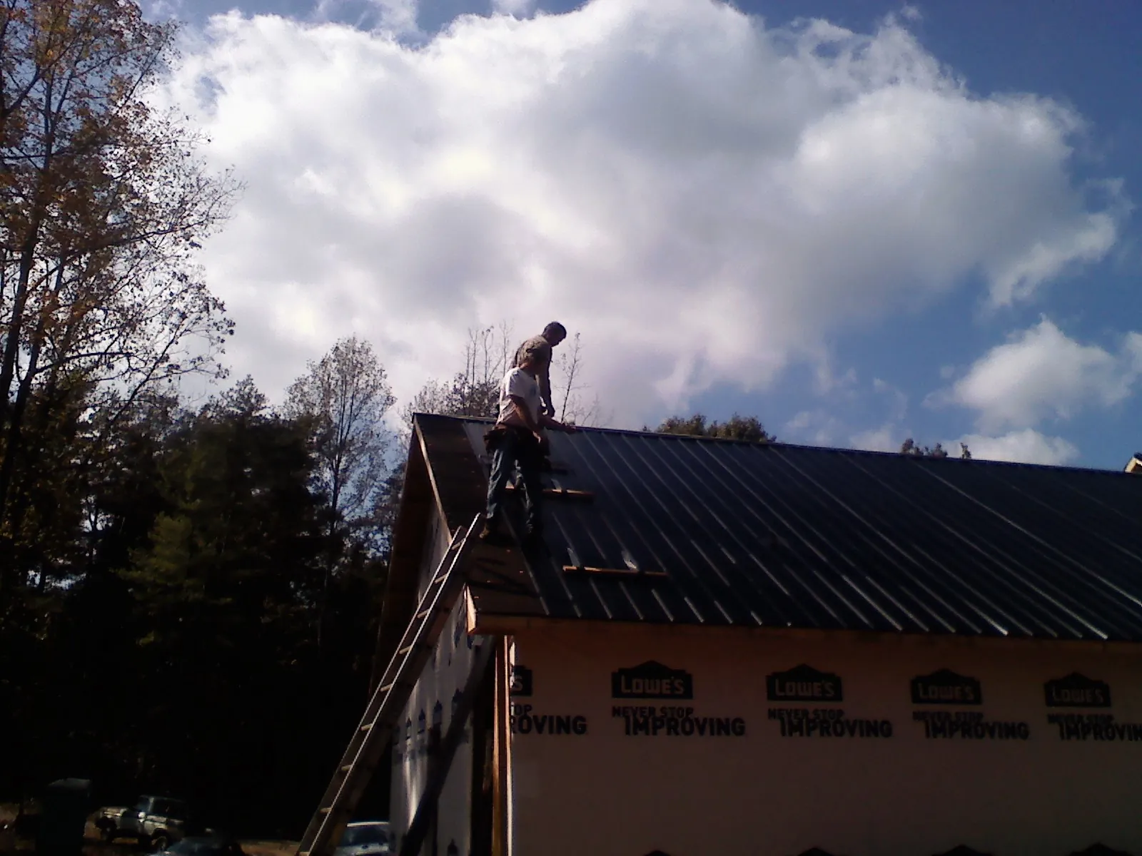 Roofer fastening dark metal panels high against a cloudy sky, from a Roof Inspection job in Alger