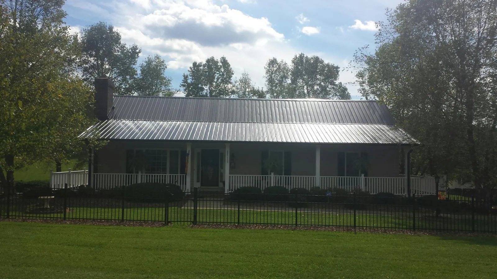 Gray metal roof on a brick ranch with a full width front porch — Gutter Guard Installation work by our crew in Alger