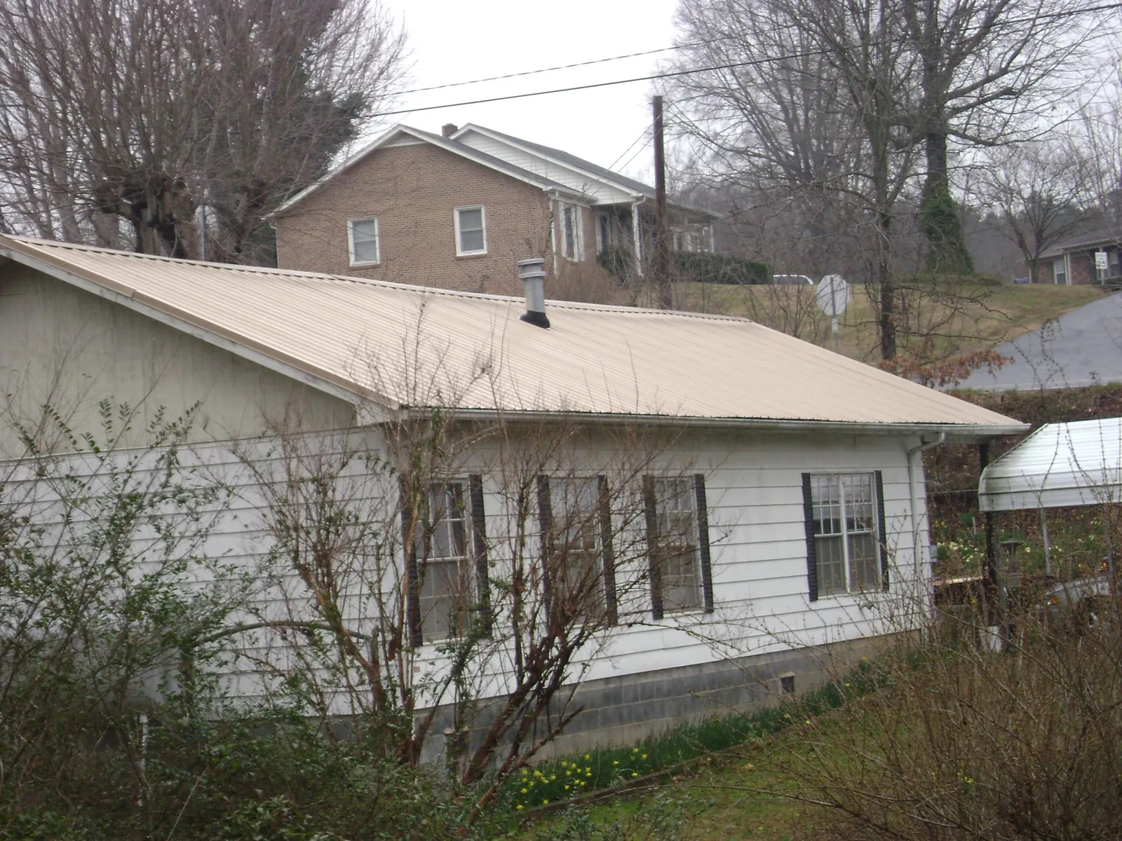 Tan metal roof on a white sided house set into a hillside — Commercial Roofing by Roofing Brothers in Alger