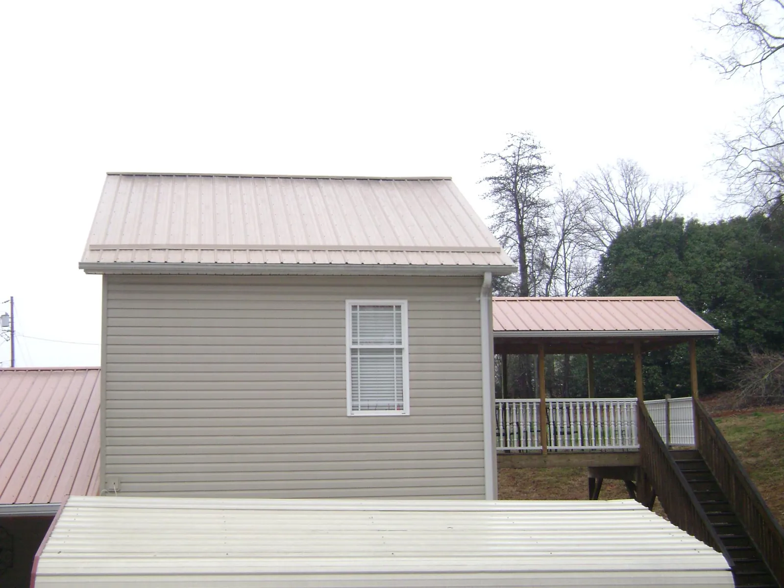Tan metal roofs on a two story addition and attached porch, from a Roof Replacement job in Alger